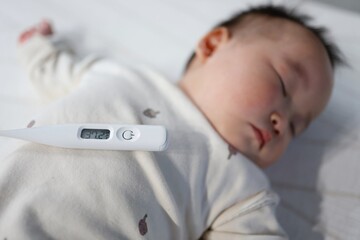 眠る赤ちゃんと体温計の平熱表示37.2度。