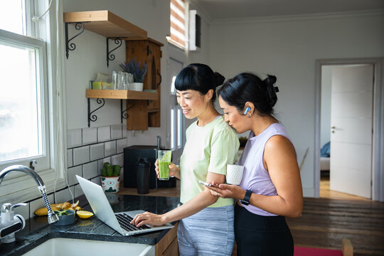 Adult lesbian couple smiling at laptop in home kitchen