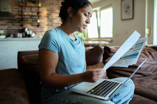 Adult woman reviewing bills on laptop at home, concerned
