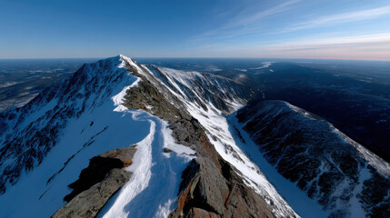 A stunning aerial view showcasing a snow-covered mountain peak against a backdrop of endless valleys and blue skies, highlighting nature's breathtaking beauty and grandeur.