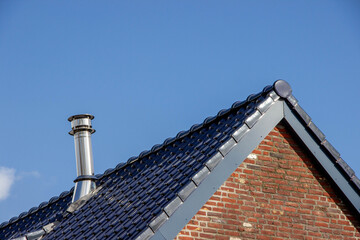 Roof of a residential building featuring a chimney, blue tiles, and a clear sky in the background, showcasing architectural design and craftsmanship in construction
