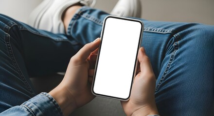 Close-up of a person holding a smartphone with a blank white screen in their hands, wearing blue jeans and a denim shirt.