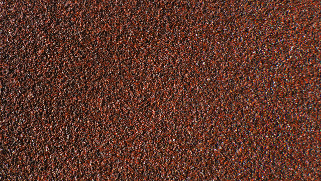 Close-up of abrasive sandpaper texture in a maroon color. Detailed background of a rough granular material for construction and renovation