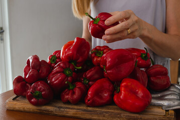 Woman's hand selecting red bell peppers on a wooden cutting board.