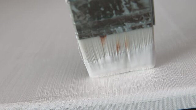 Close up of an artist priming canvas with white ground, preparation for painting. Selective focus