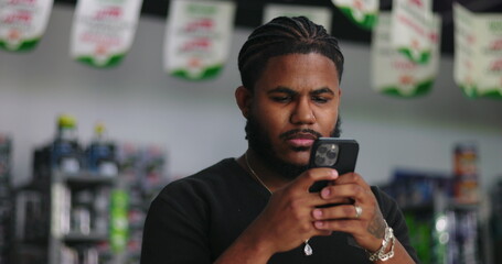 Young man of African descent intently focused on smartphone screen in a store environment, illustrating digital engagement and modern reliance on technology