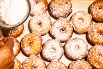 The cook is sprinkling powdered sugar on fried donuts.