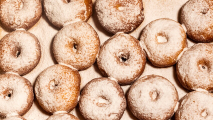 The cook is sprinkling powdered sugar on fried donuts.