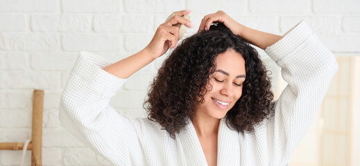 Young African-American woman using massage brush for hair growth in bathroom