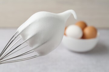 Whisk with whipped egg whites on blurred background, closeup. Space for text