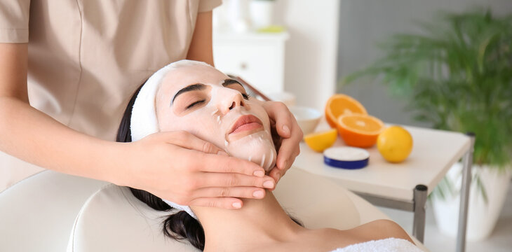 Cosmetologist applying sheet mask on woman's face in beauty salon - Powered by Adobe