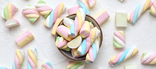 Bowl with tasty twisted marshmallows on light background