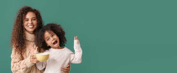 Naklejka premium African-American woman and her little daughter with mug of cocoa on green background