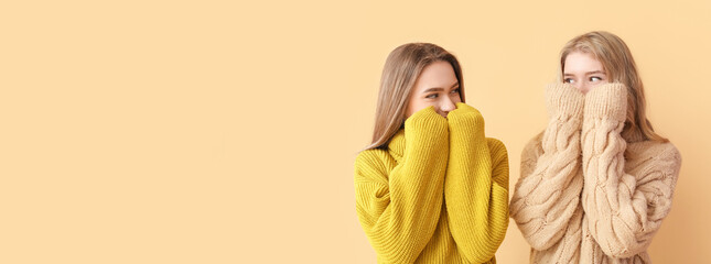 Portrait of young sisters in warm sweaters on color background