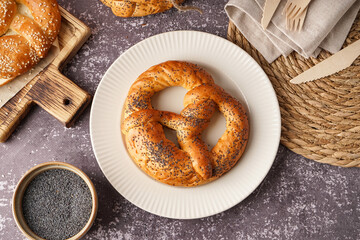 Plate with tasty pretzel and poppy seeds on grunge background