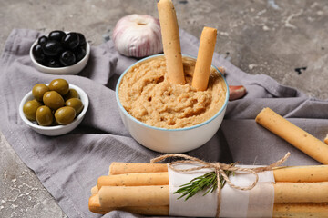Bowls with hummus, olives and bunch of tasty Italian Grissini on grunge background