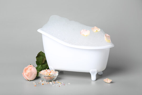 Small bathtub with foam, sea salt and rose flower on light background