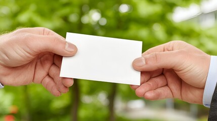 Person handing over a blank white business card with a green leafy background promoting communication now.
