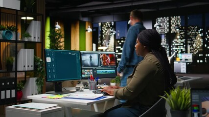 Female specialist editor working in video production industry at agency office, doing color grading and creating a montage on dual monitors. Creative process with multimedia tech tools. Camera A.
