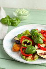 Plate with grilled vegetables and basil on green wooden table
