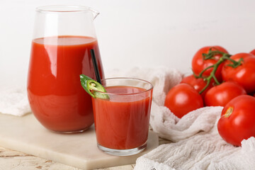 Glass and jug of tasty tomato juice on white wooden background