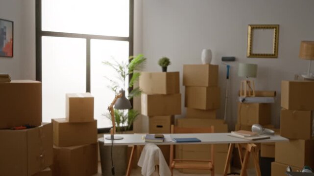Moving day scene with stacked cardboard boxes, studio desk and lamp in a defocused shallow bokeh background interior; background backplate copyspace calm.