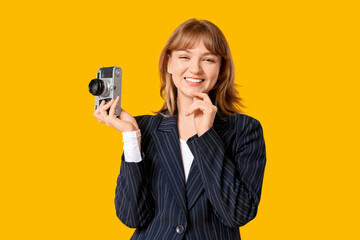 Beautiful young woman with retro camera on yellow background