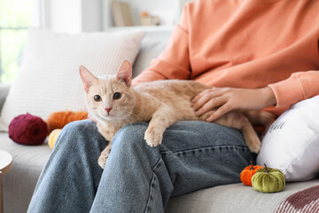 Young man with cute cat sitting at home on autumn day, closeup