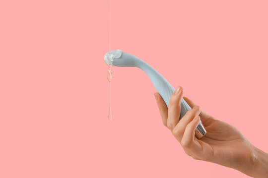Woman holding vibrator with lubricant on pink background