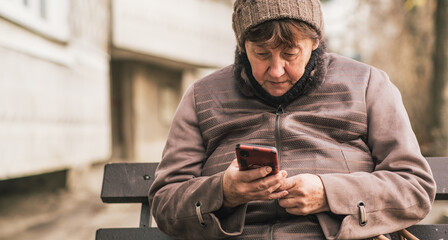Elderly woman sitting on a bench using a smartphone in an urban setting during the day