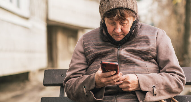 Elderly woman sitting on a bench using a smartphone in an urban setting during the day