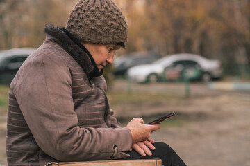 Elderly woman sitting on a bench using a smartphone in an urban setting during the day