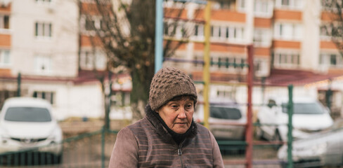 Elderly woman sitting on a park bench wearing a knitted hat during a cool autumn day in an urban setting