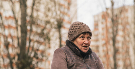 Elderly woman sitting on a park bench wearing a knitted hat during a cool autumn day in an urban setting