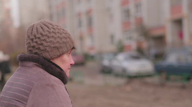 Elderly woman outdoors wearing a brown hat and jacket, expressing thoughtful contemplation during a chilly afternoon