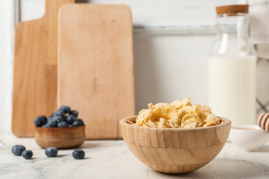 Bowl with tasty cornflakes, blueberries and bottle of milk on light background