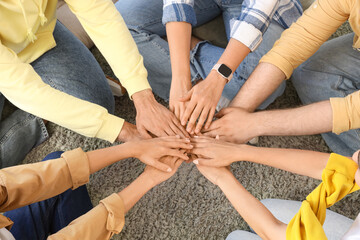 Young people putting hands together on carpet at group therapy session, top view