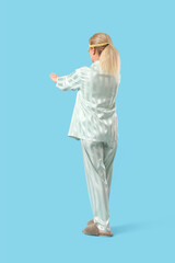 Female sleepwalker in pajamas on blue background, back view