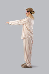 Female sleepwalker in pajamas on grey background