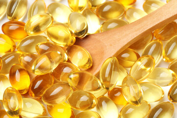 Wooden spoon with many vitamin E capsules as background