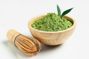 Bowl with powdered matcha tea, chasen and fresh leaves on beige background