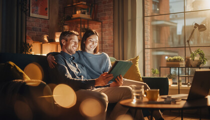 Happy couple sitting on cozy sofa in modern living room, smiling while checking investment portfolio on digital tablet, warm evening light, relaxed atmosphere