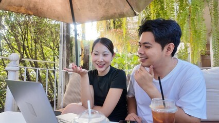 A man and a woman are sitting at a table with a laptop and a cup of tea