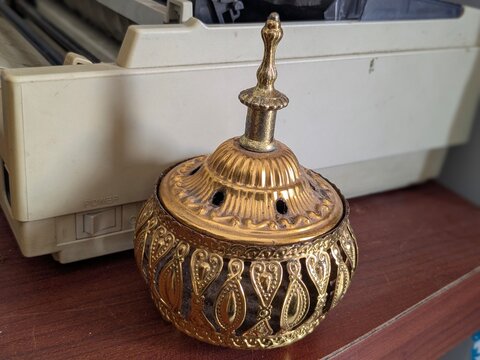 Ornate golden metal incense burner with intricate patterns and a finial on a wooden surface. - Powered by Adobe