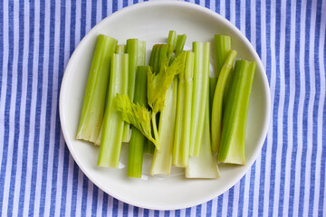 Fresh celery stalks cut into short pieces on a striped cloth.