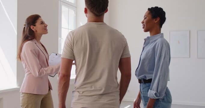 Confident female realtor or real estate agent greets family couple for room tour of new home, guiding clients through property, offering professional insight, showcasing potential.
