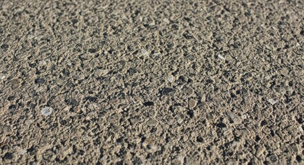 Closeup texture of rough, grey asphalt with visible aggregate and small stones, showing a gritty surface