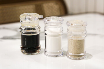 Close-up of soy sauce, salt, and pepper in clear glass shakers. Classic table condiment trio for seasoning at restaurants or home dining.