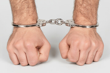 Two hands are bound by metal handcuffs, symbolizing restraint and law enforcement.