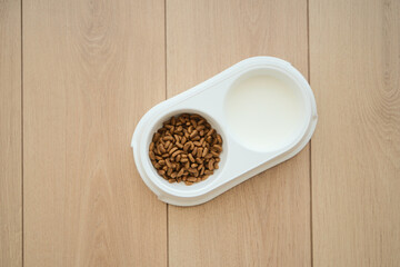 Pet food bowl with dry kibble and milk placed on wood floor
